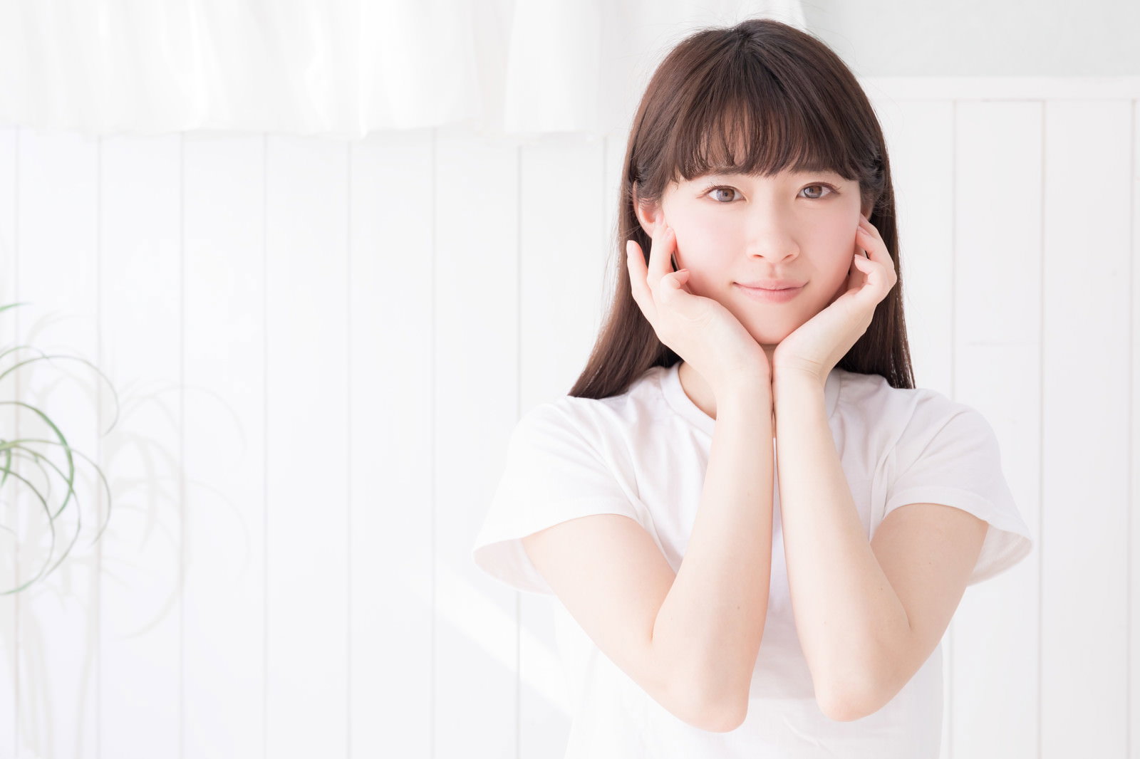 白い壁の前で白いTシャツを着た女性が両手で顎を支えるポーズをとっている［モデル：川子芹菜］