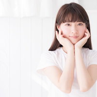 白い壁の前で両手で顎を支える色白女性のスキンケアの写真
