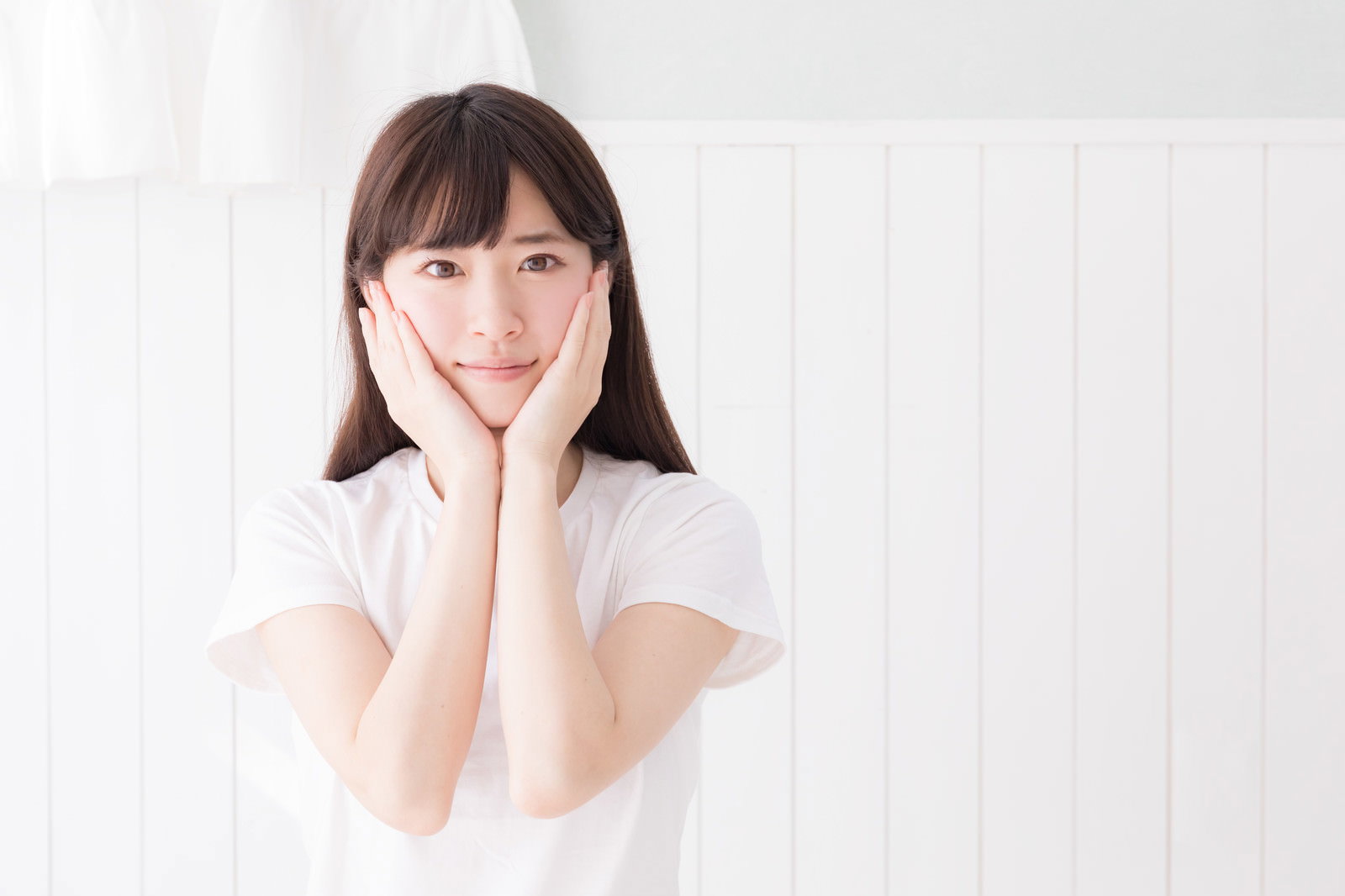 白いTシャツを着た色白の女性が両手を頬に添えている様子［モデル：川子芹菜］