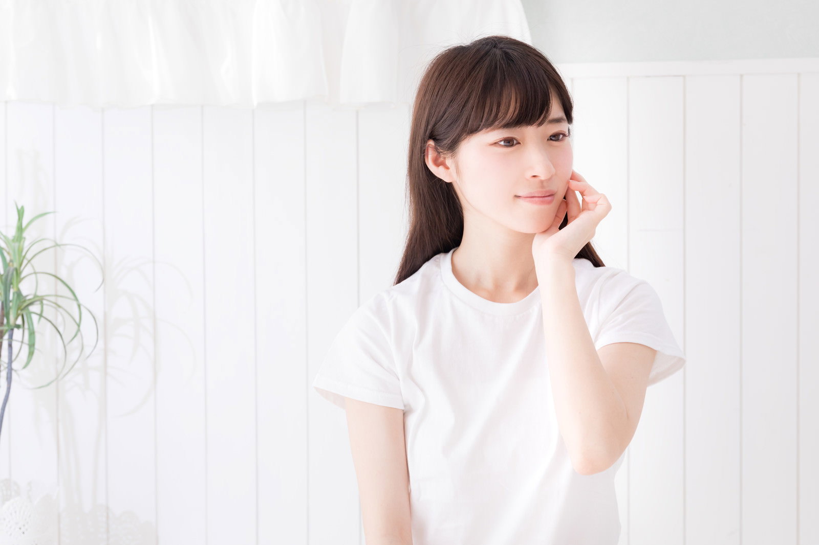 頬に手を当てて穏やかな表情を見せる白Tシャツの女性