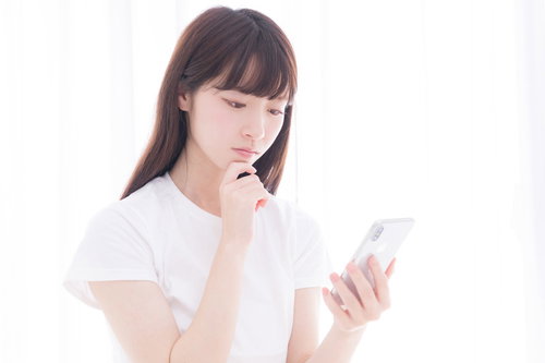 スマホを眺めて考え込む白いTシャツの女性