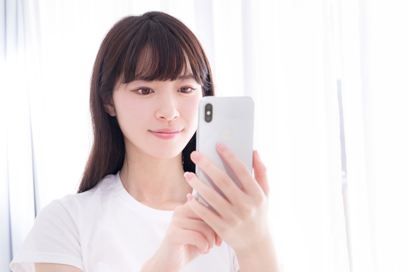 白いTシャツを着た女性がスマートフォンを操作している［モデル：川子芹菜］