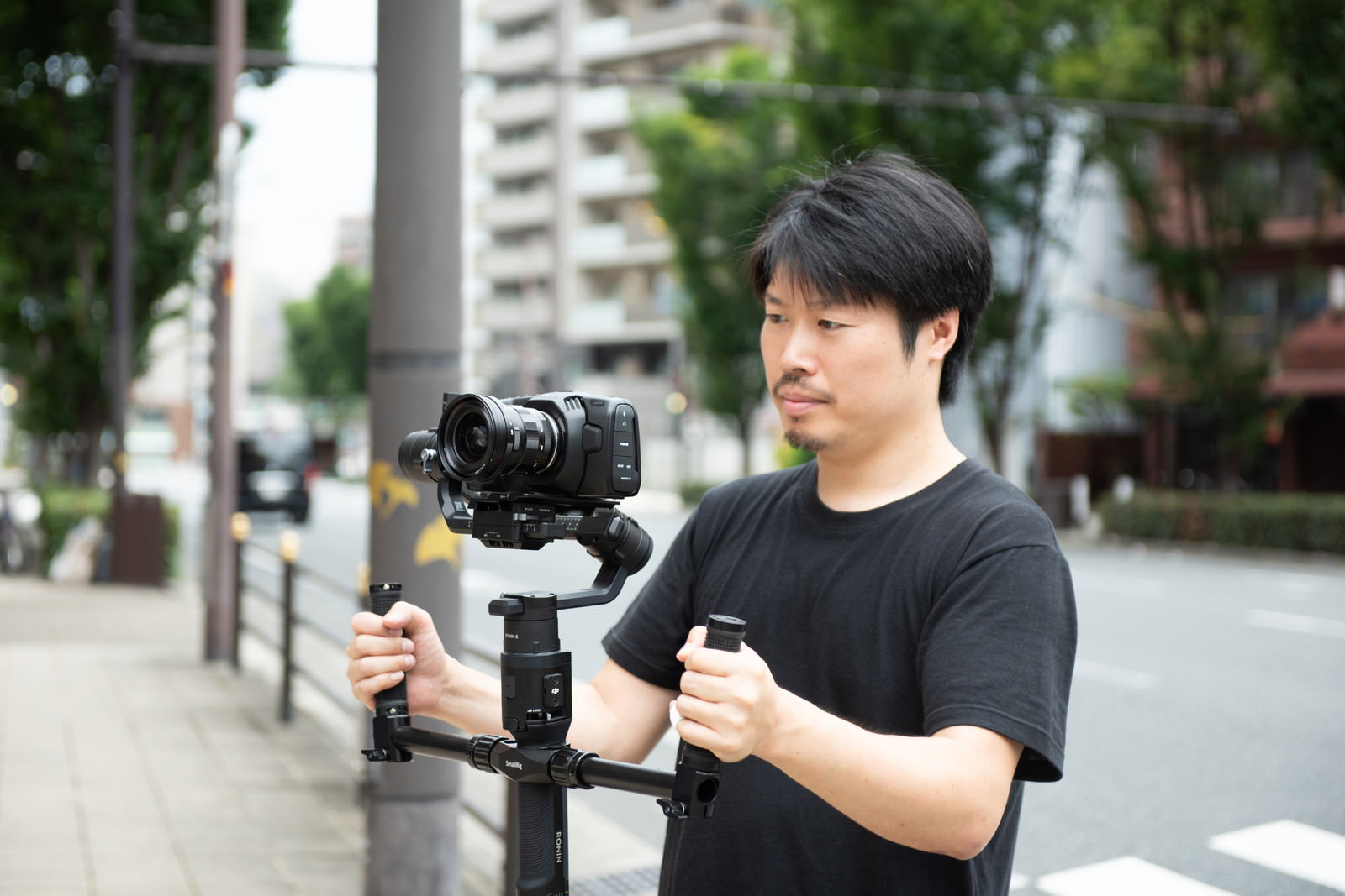 ジンバルを使って屋外で動画撮影をしている黒いTシャツの男性カメラマン［モデル：瀧野恵太］