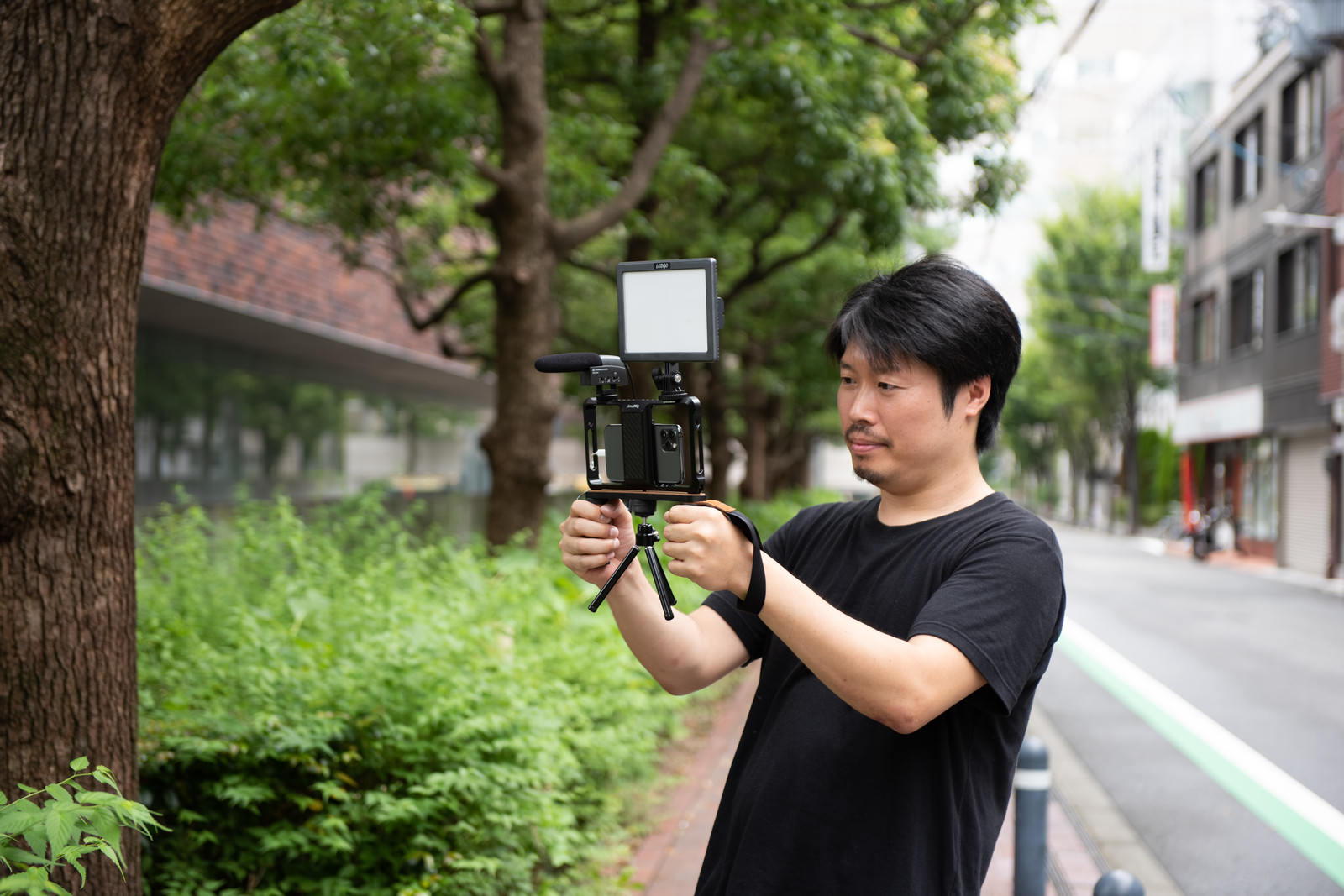 屋外でスマートフォンにマイクを取り付けて動画撮影する黒いTシャツの男性［モデル：瀧野恵太］