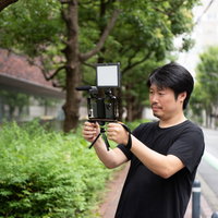 屋外でスマートフォンにマイクを取り付けてムービー撮影する男性の写真