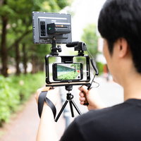 野外ロケで三脚にスマートフォンをセットして撮影する男性の写真