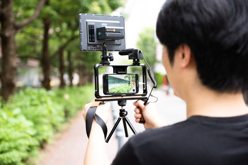 野外ロケで三脚にスマートフォンをセットして撮影する男性