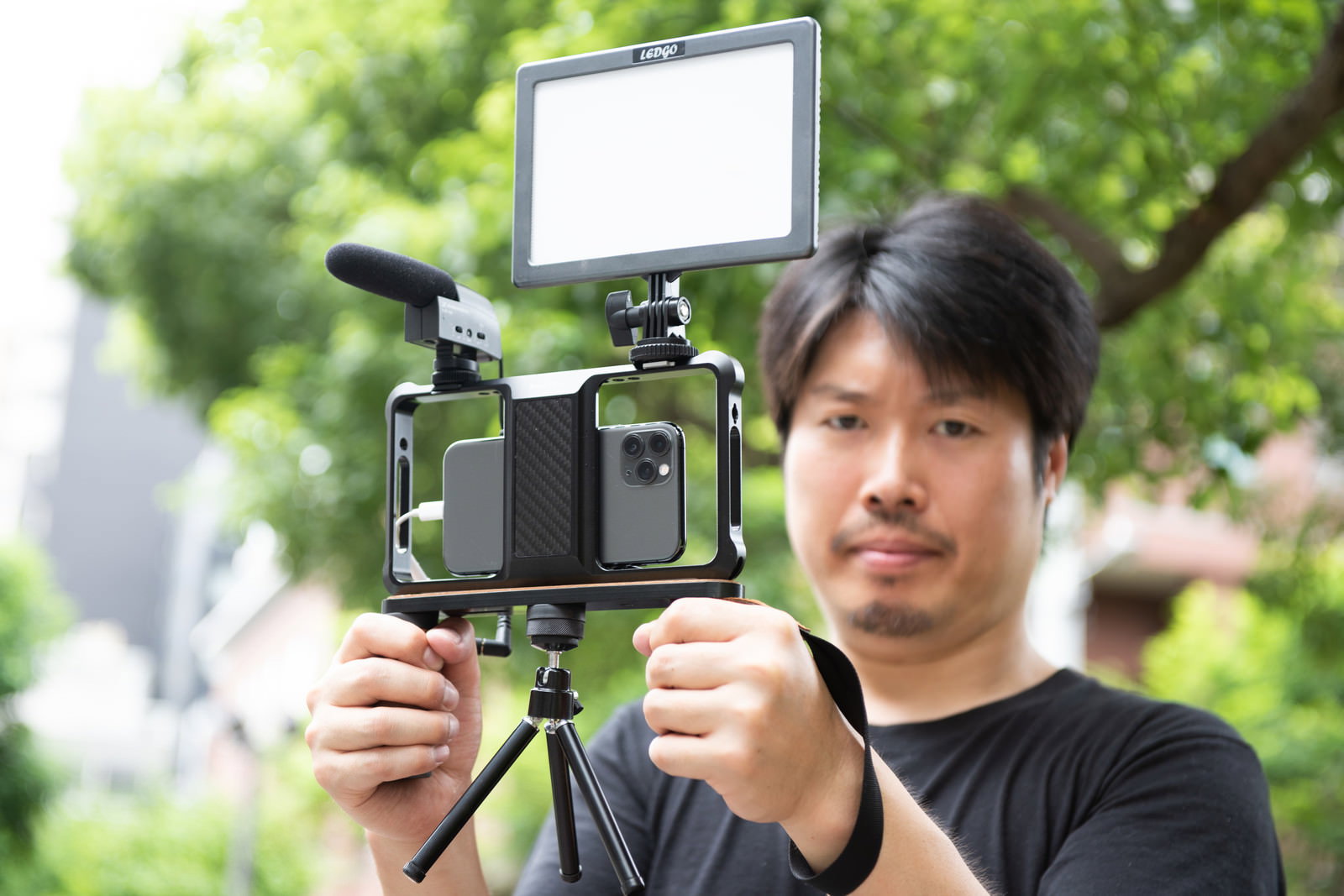 屋外でスマートフォンにマイクを装着して動画撮影をする黒いTシャツの男性［モデル：瀧野恵太］
