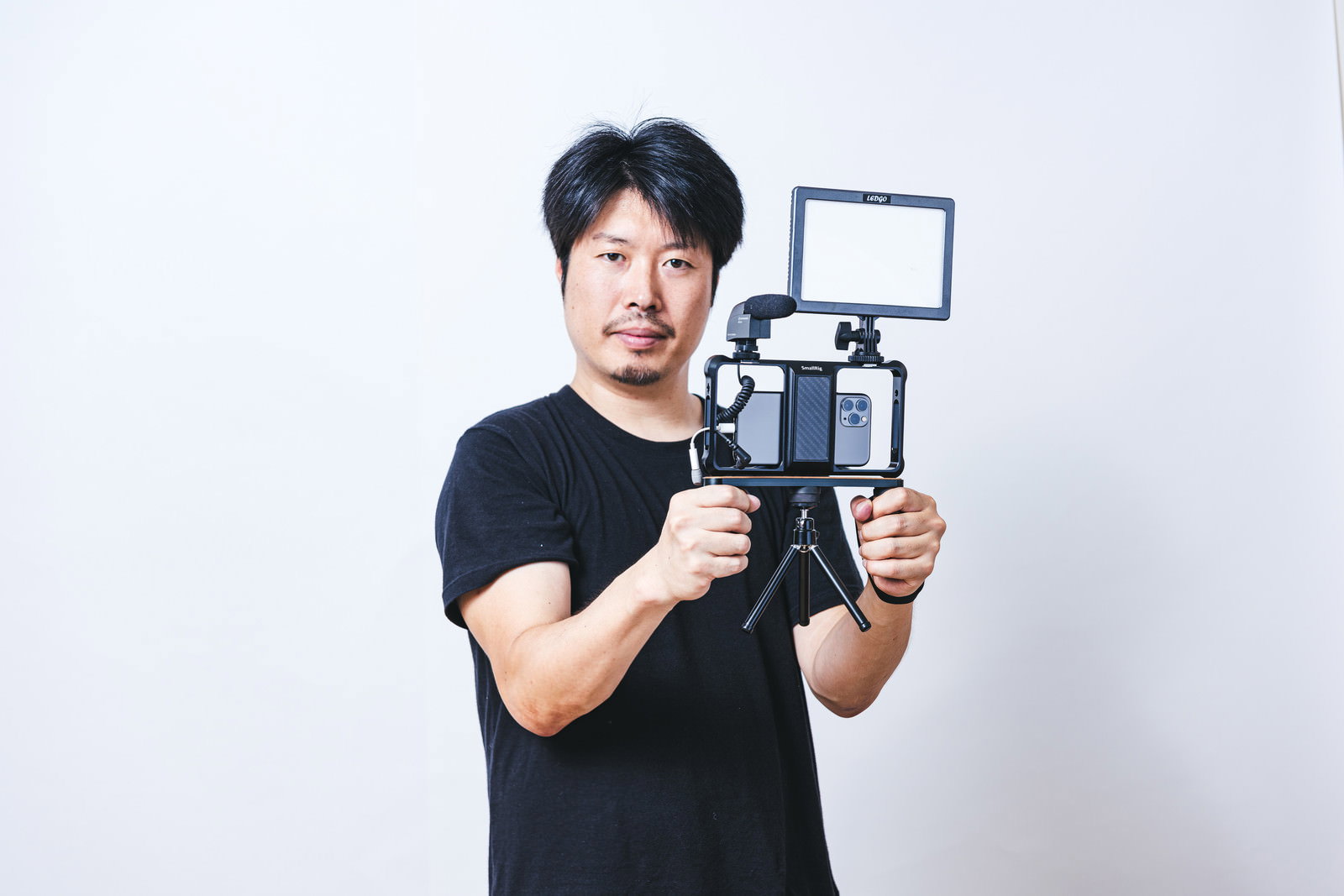 照明機材付きのスマートフォンを持って撮影準備をする黒いTシャツの男性［モデル：瀧野恵太］