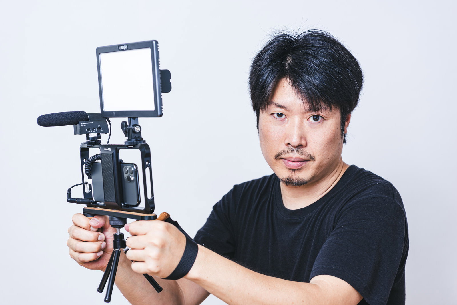 スマートフォンを三脚に固定して照明を使い動画撮影する黒Tシャツの男性カメラマン［モデル：瀧野恵太］