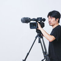 三脚に設置したビデオカメラを操作する真剣な眼差しのカメラマンの写真