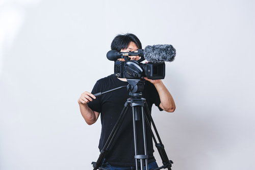 三脚に設置したビデオカメラで水平方向にパンをするカメラマン