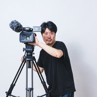 三脚に設置したビデオカメラで撮影収録中のカメラマンの写真