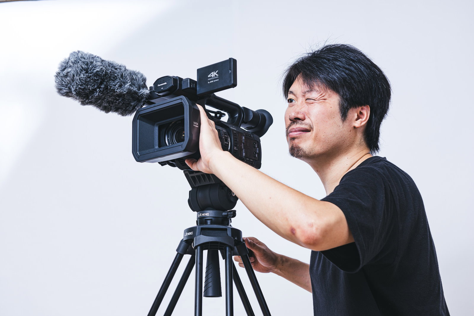 片目を閉じてビデオカメラのファインダーを覗き込みながらムービー撮影をする黒いTシャツの男性［モデル：瀧野恵太］