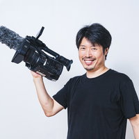 業務用ビデオカメラを片手で持ち上げる笑顔の男性カメラマンの写真