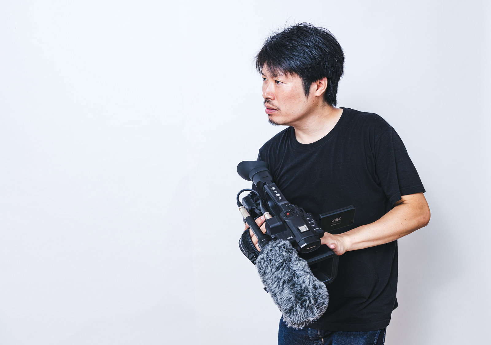 ビデオカメラを持ってスタンバイしている黒いTシャツの男性カメラマン［モデル：瀧野恵太］