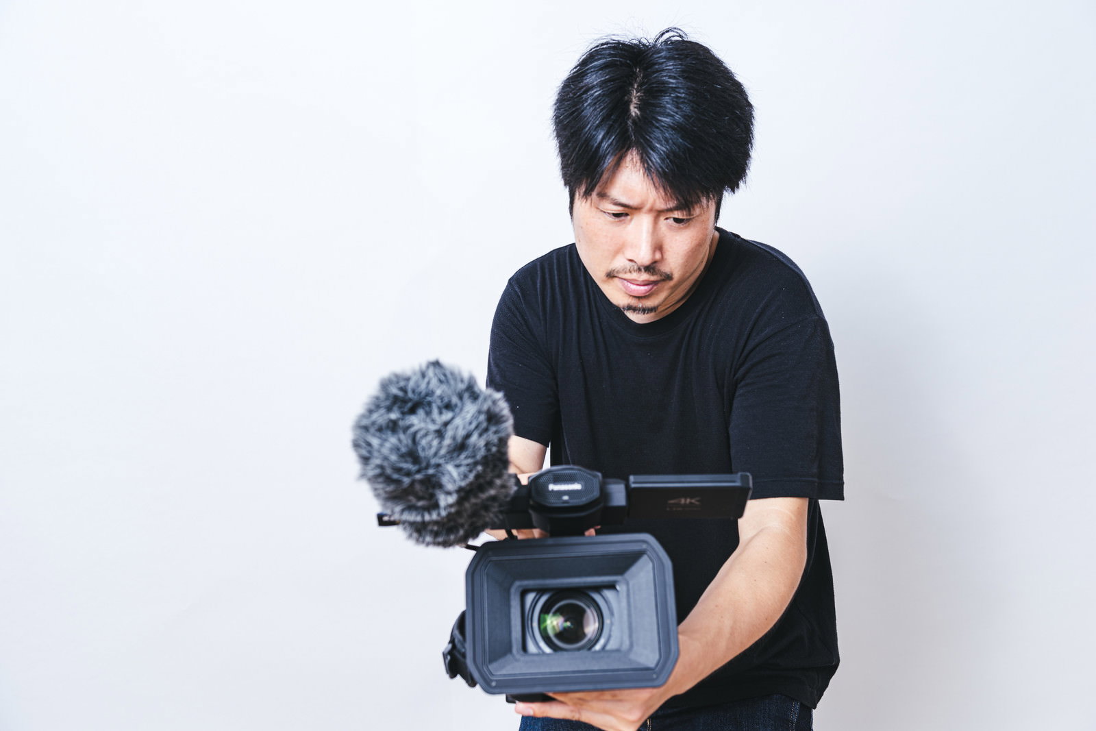 ローアングルでハンディビデオカメラを構えて撮影する黒いTシャツの男性［モデル：瀧野恵太］