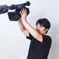 両手を伸ばして高い位置からムービー撮影する男性カメラマンの写真