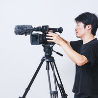 三脚に業務用4Kビデオカメラを取り付けるカメラマン男性の写真