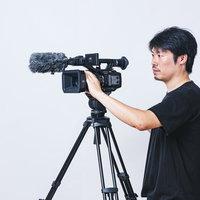 アイレベルで三脚のビデオカメラを操作するカメラマン男性の写真