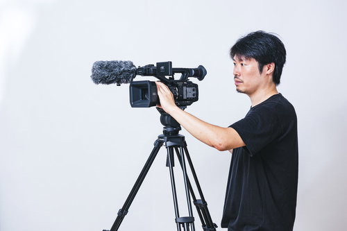 アイレベルで三脚のビデオカメラを操作するカメラマン男性