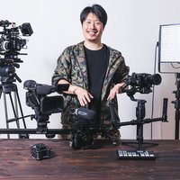 動画機材に囲まれてポーズをとる男性カメラマンの写真