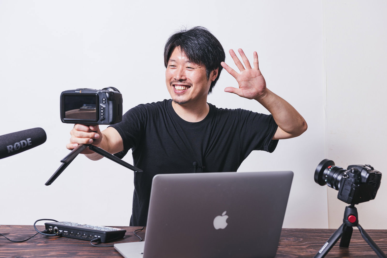カメラを持って手を振り笑顔でパフォーマンスするYouTuber男性［モデル：瀧野恵太］