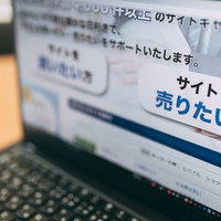 デスクのノートパソコンで表示するサイト売買・仲介情報の写真
