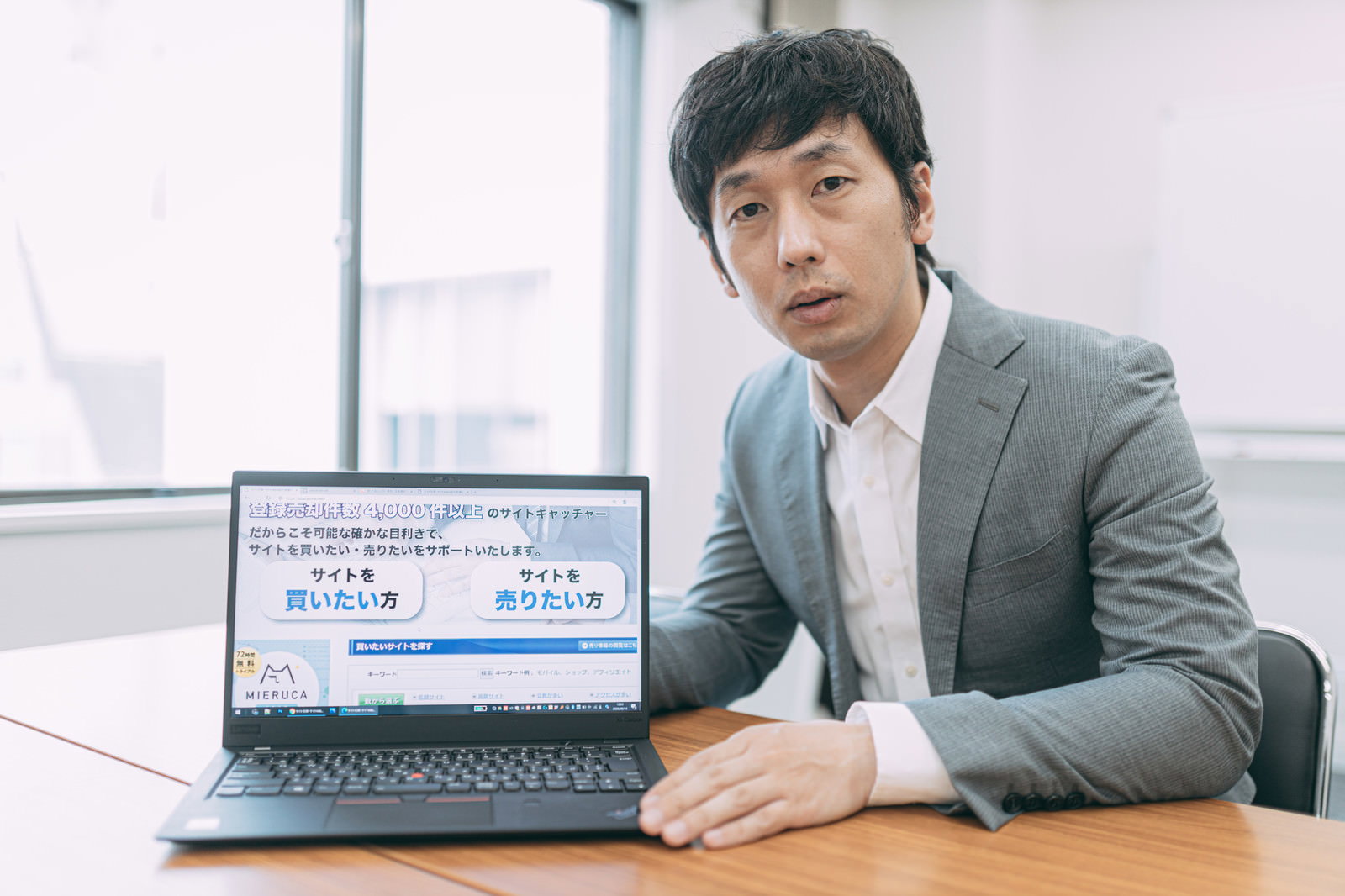 ノートパソコンでプレゼンテーションするグレーのスーツの男性［モデル：大川竜弥］