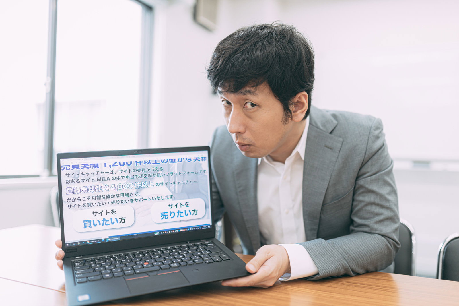 グレーのスーツを着た男性がデスクでノートパソコンを操作している［モデル：大川竜弥］