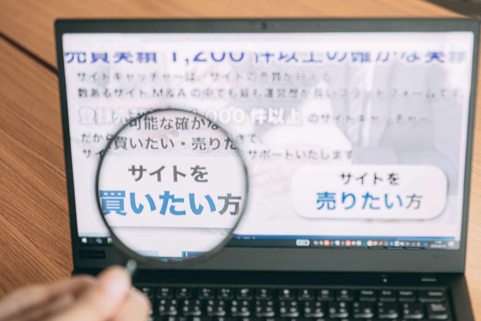虫眼鏡を使ってノートパソコンの画面を詳しく見ている男性