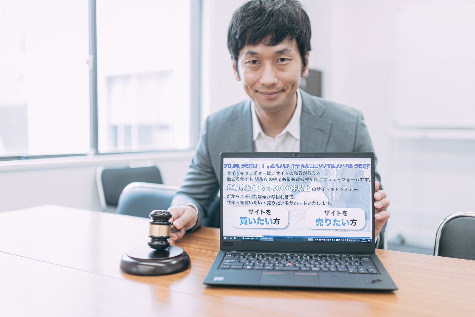 オフィスでノートパソコンを見せる笑顔のスーツ姿の男性［モデル：大川竜弥］