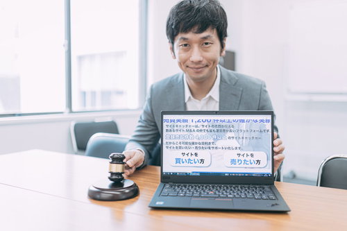 サイト売買成立時のオフィスでノートパソコンを見せるスーツ姿の男性