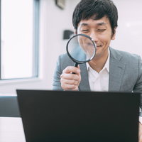 ノートパソコンの画面を虫眼鏡で鑑定する男性の写真