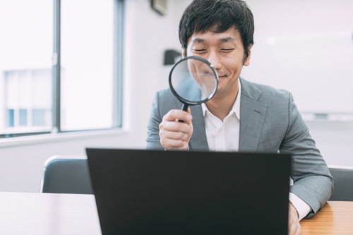 ノートパソコンの画面を虫眼鏡で鑑定する男性