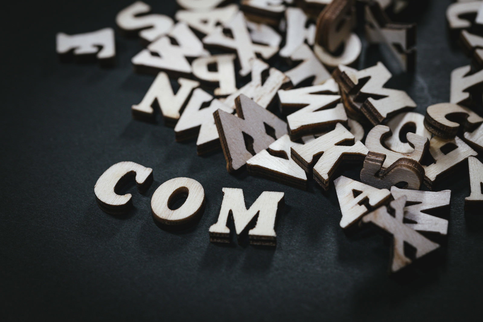 暗い背景に散らばる白い木製アルファベットとCOMの文字