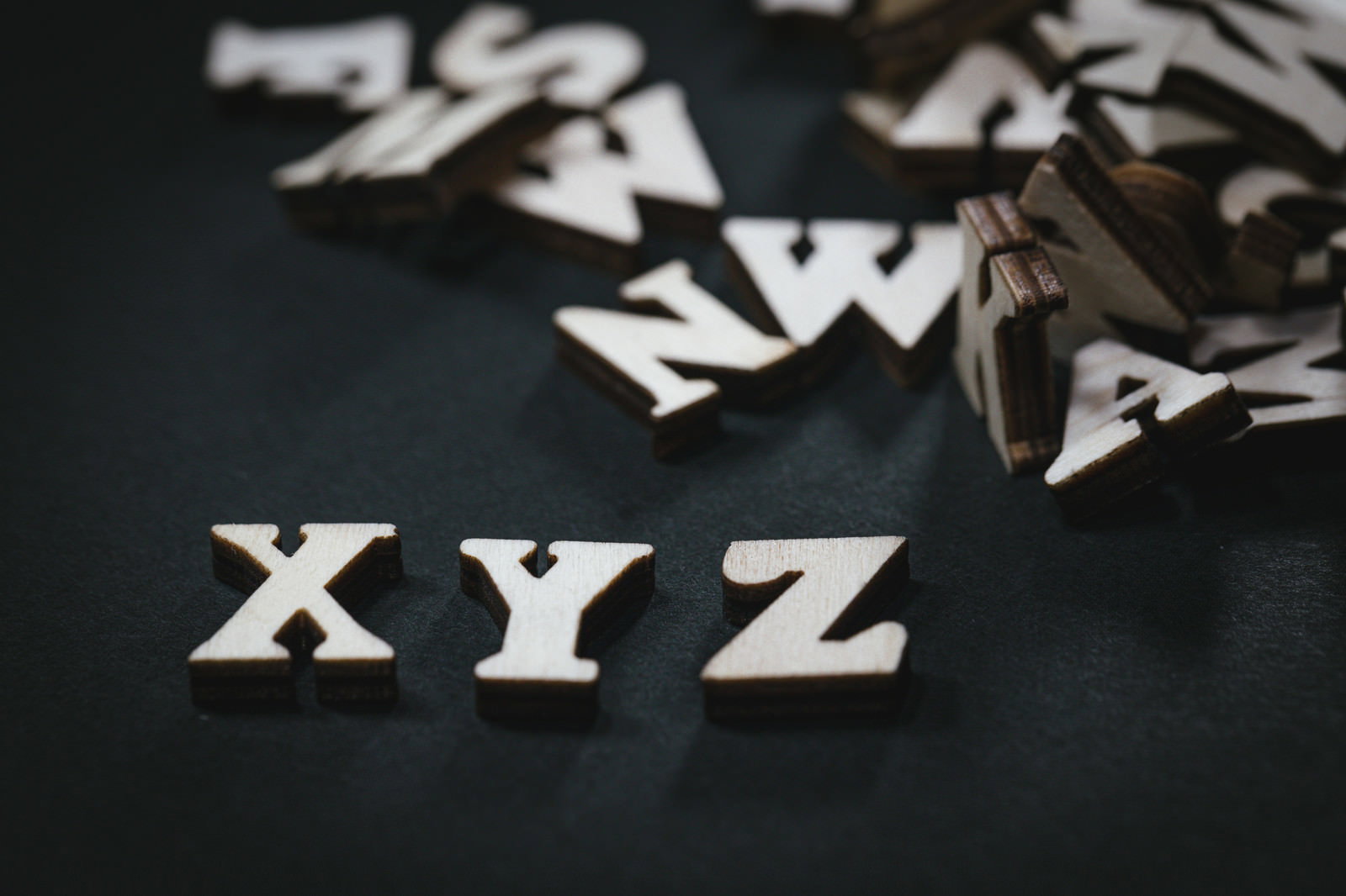 Wooden English letter blocks scattered on a black background with the letters XYZ in the foreground