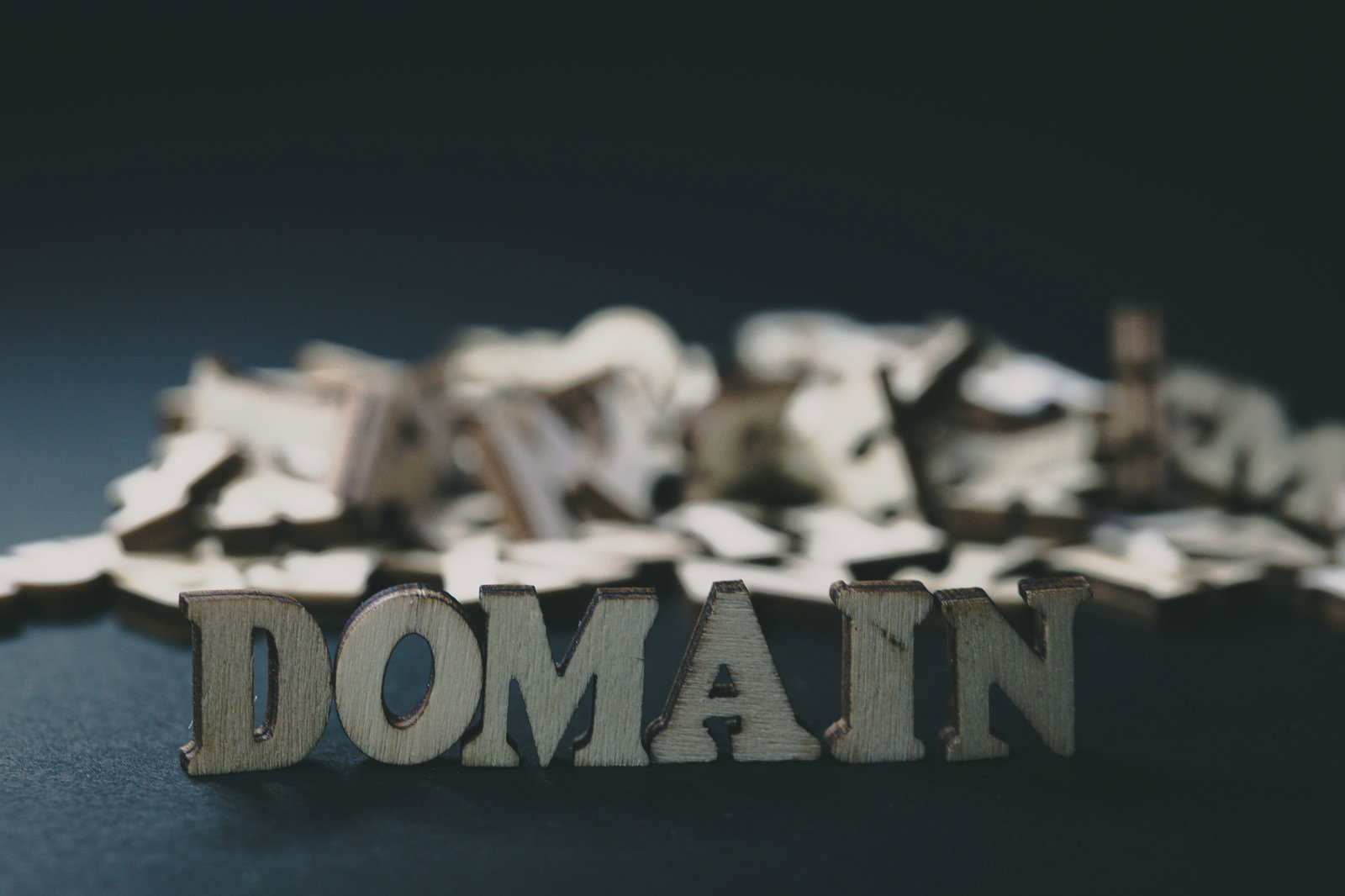 木製の英文字でDOMAINと表現され背景に散らばったアルファベット