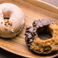 木のお皿に乗ったドーナツ2個、白いグレーズとチョコレートコーティングの写真