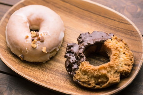 木のお皿に乗ったドーナツ2個、白いグレーズとチョコレートコーティング