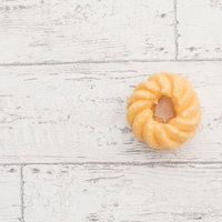 白い木目調の背景に置かれた黄金色のフレンチクルーラーの写真