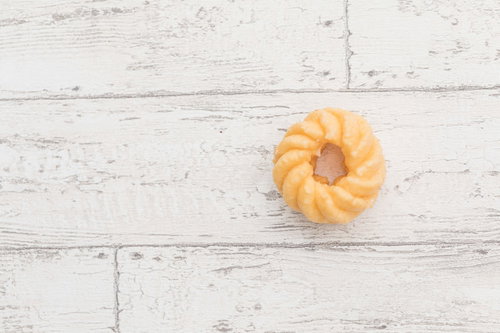 白い木目調の背景に置かれた黄金色のフレンチクルーラー