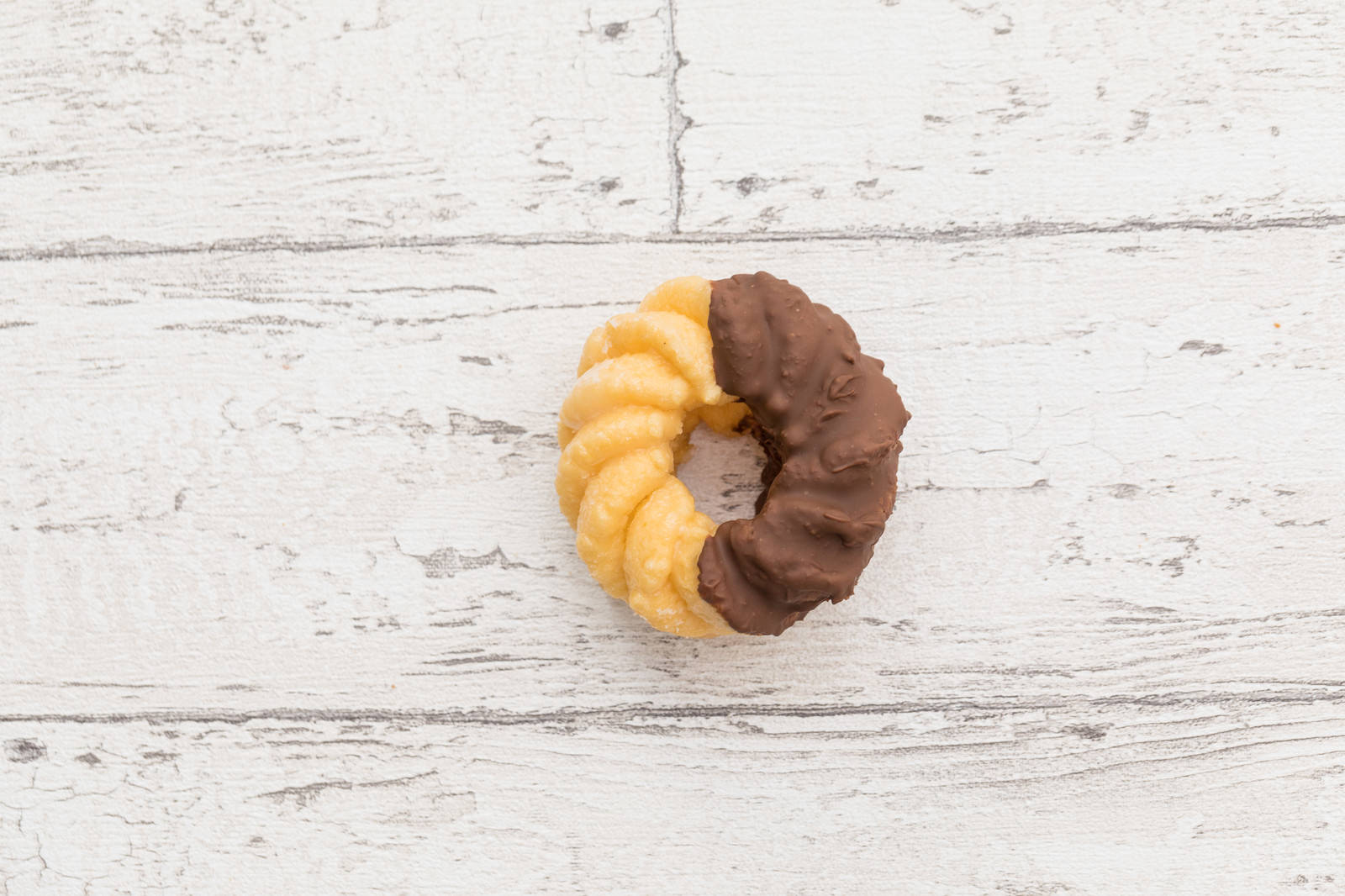 白い木目背景に置かれたチョコレート色と薄黄色のフレンチクルーラー