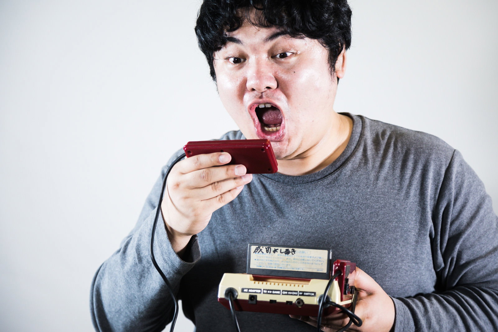ファミコンのコントローラーを持って大きく口を開けて叫ぶ男性［モデル：段田隼人］