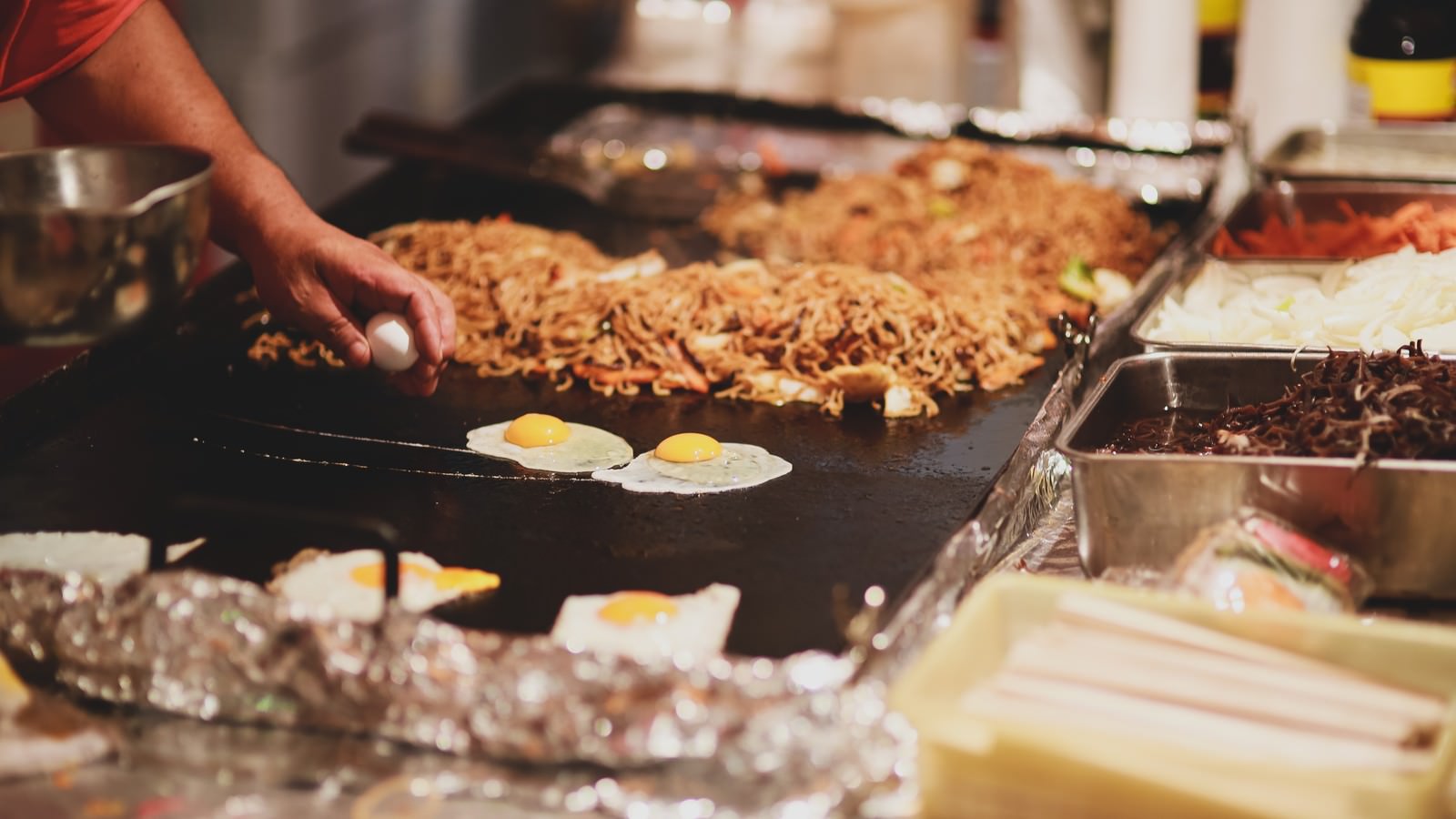 屋台の鉄板で広島風お好み焼きを調理する調理人の手元