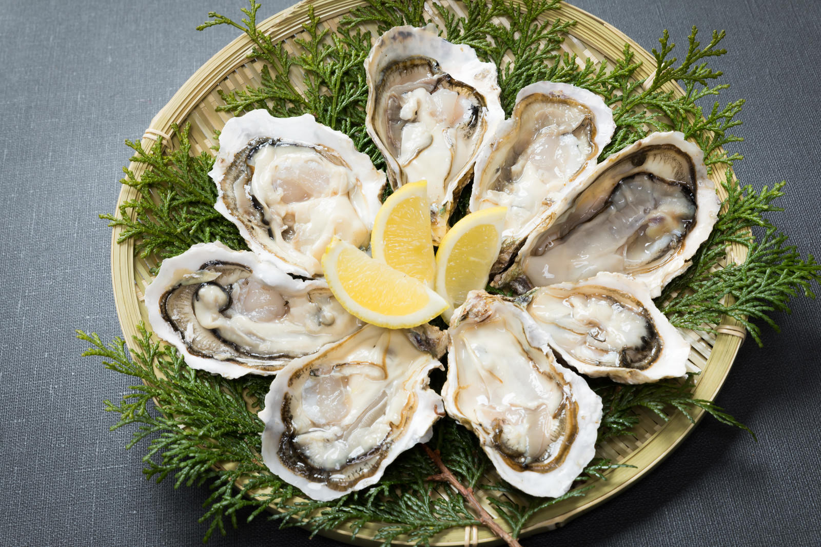 檜葉を敷いたザルの上に並べられた8個の恵比須牡蠣とレモン