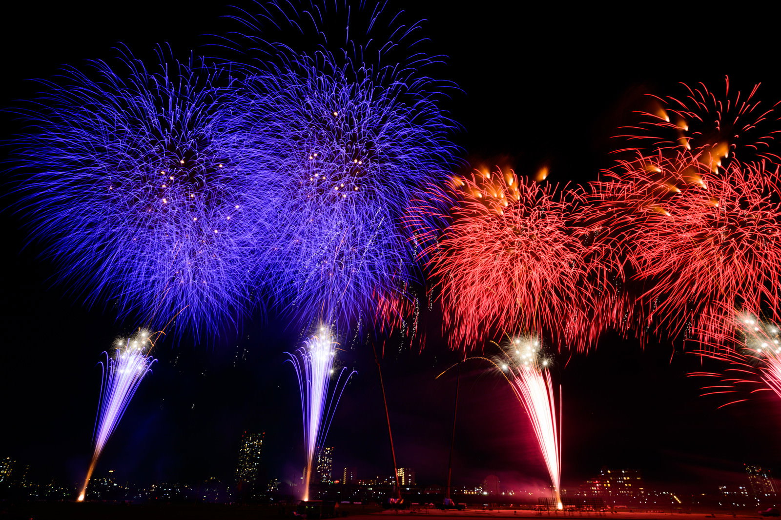 夜空に青色と赤色の花火が左右に分かれて打ち上がる様子
