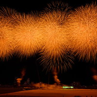 夜空に連続で打ち上がるオレンジ色のスターマイン花火の写真