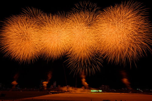 夜空に連続で打ち上がるオレンジ色のスターマイン花火