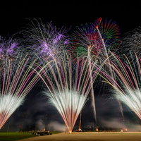 夜空に扇状に噴き上げる打上花火の光跡が放射状に広がる様子の写真